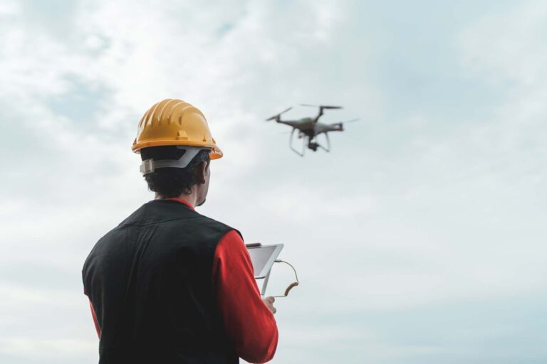 Bauingenieur in gelbem Helm bedient Tablet mit fliegender Drohne im Hintergrund für PB-TGA Bauplanung